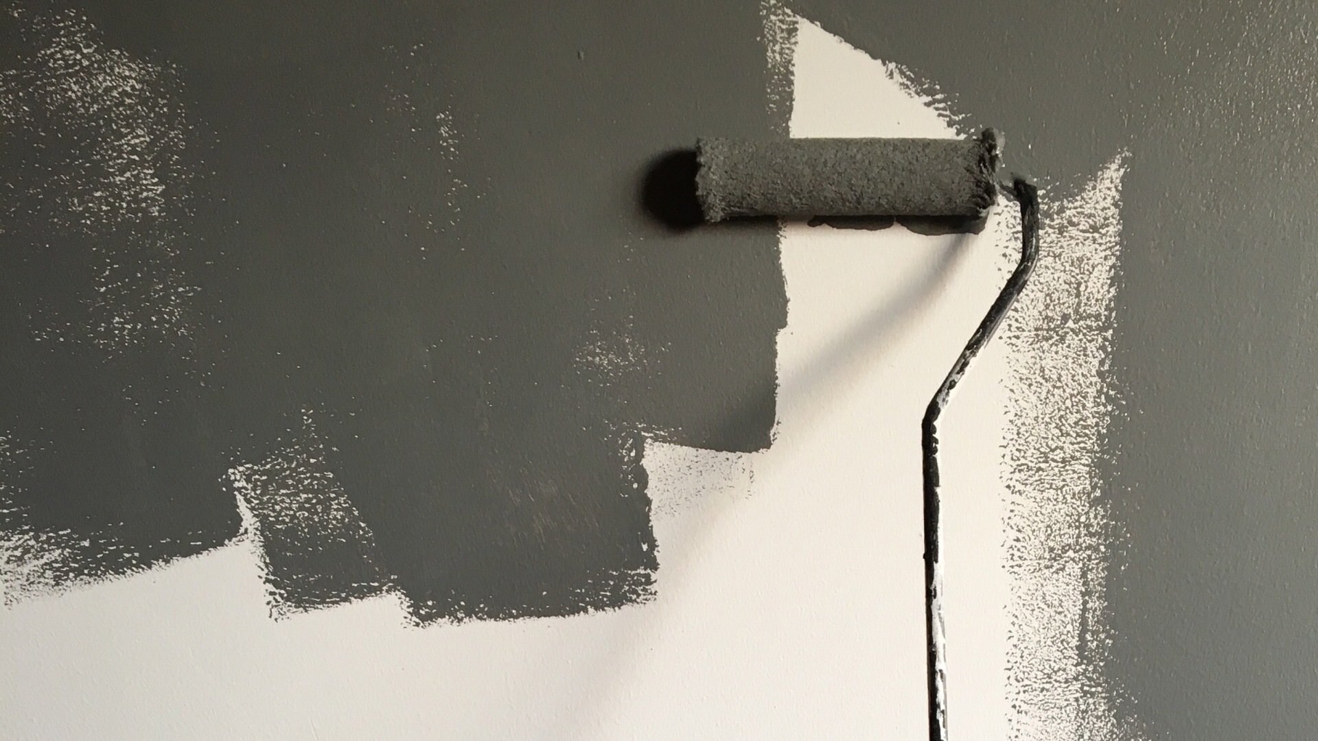 A roller laying fresh gray paint on a wall
